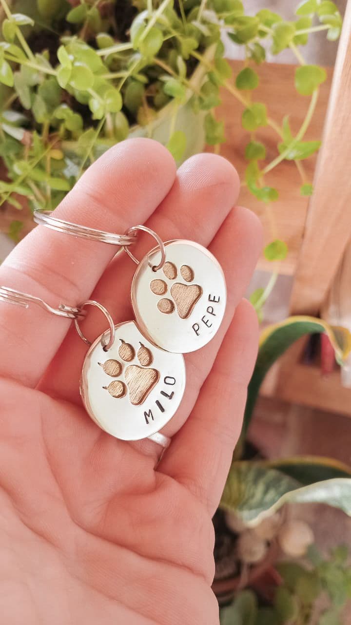 Chapita identificatoria hecha a mano sobre alpaca con huellita calada, lleva nombre al frente y teléfono al reverso